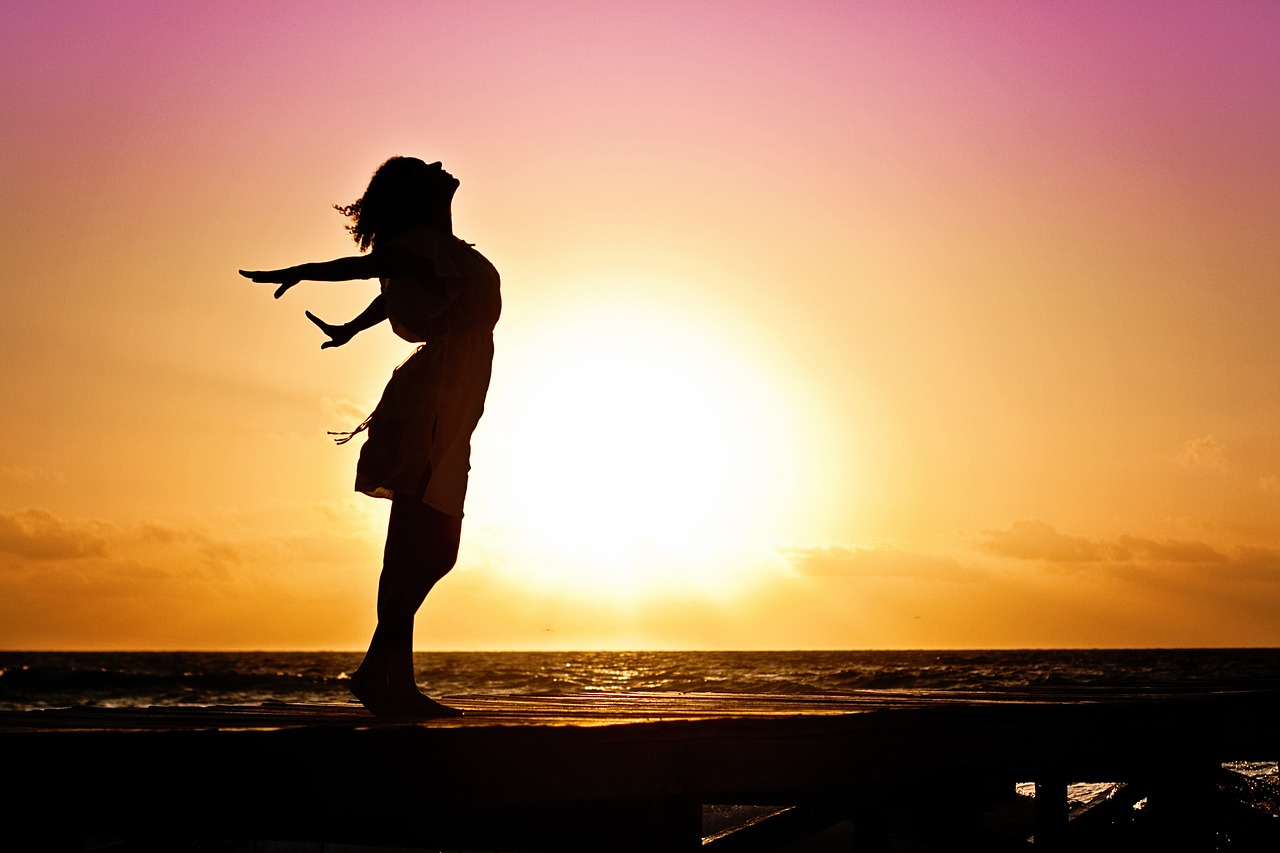 woman standing beside the ocean at sunset doing breathing excercises